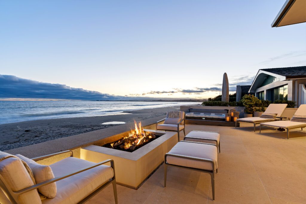A beach with chairs and fire pit on the sand.